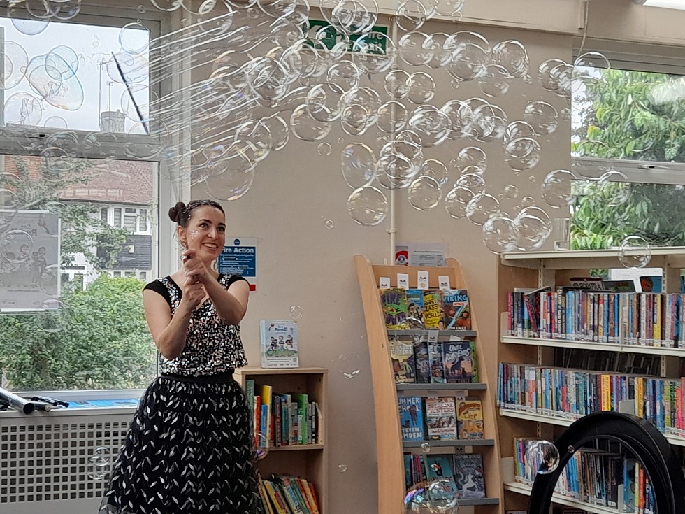 Woman blowing bubbles with bubbles around her in front of library shelves